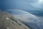 A rainbow arcs below the horizon in a glacial valley
