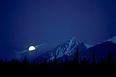 A meditative full moon rises at dusk in the mountains