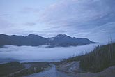 Stratus clouds hang low over a road into a valley