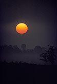 The rising sun disk glows red in the fog