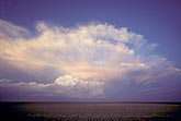 The decaying anvil cloud on a dying storm bursts in the sunset light