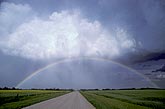 A full rainbow arcs over a country road