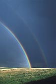 Double rainbow with dark sky over rolling hills