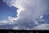 A storm cloud boils up in a changing sky, with heavy showers falling