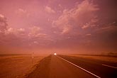 A dust storm threatens a desert highway, casting a hellish red glow
