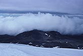 Stratus cloud banks lie on mountains behind a glacier.