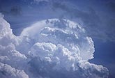 A billowing cumuliform crown rises behind small cloud fragments